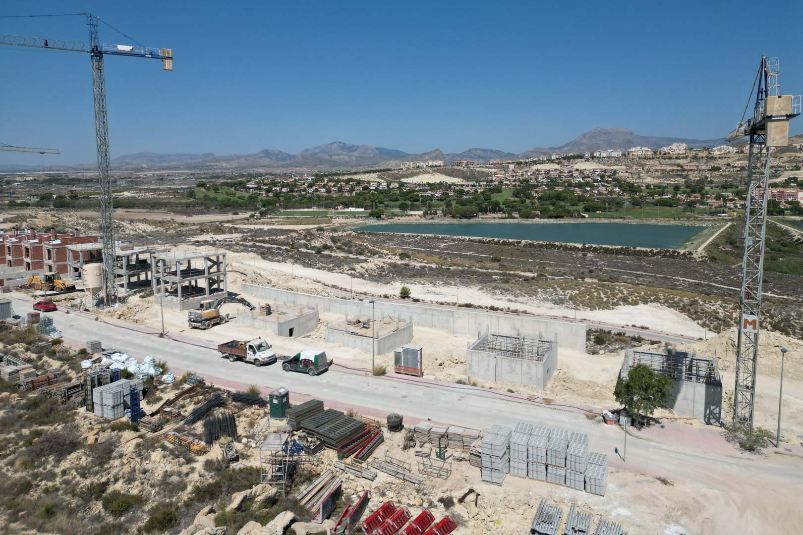 Vue aérienne du chantier des villas montrant les structures en béton, les grues et le paysage environnant avec lac et montagnes.