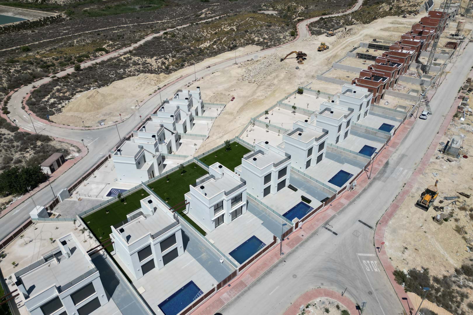 Vue aérienne du lotissement avec des villas blanches au design cubique, piscines individuelles et terrasses privées dans un secteur surélevé en plein essor.