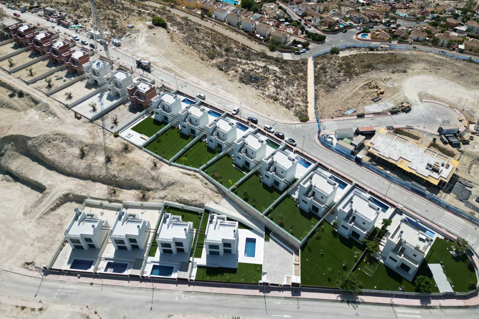 Vue aérienne d'un nouveau lotissement de villas contemporaines blanches avec piscines privées et jardins, situées sur un terrain en hauteur.