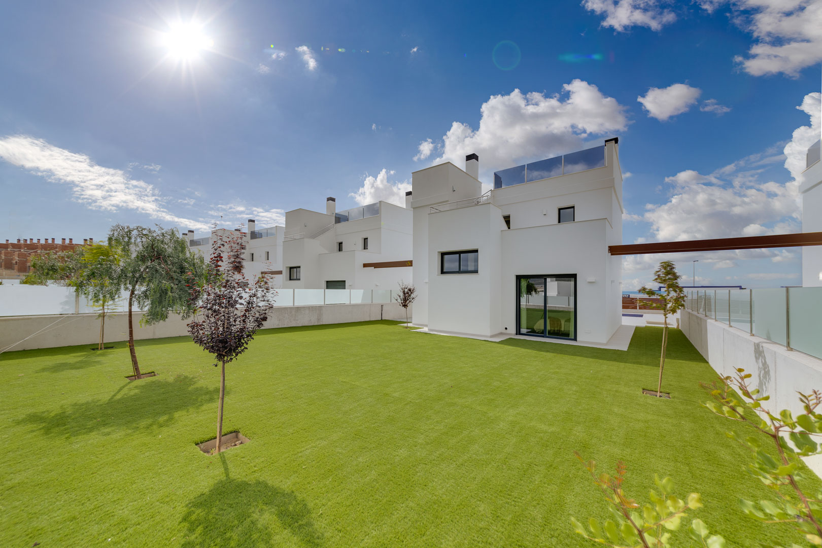Vue extérieure de la villa avec façade blanche minimaliste, vaste jardin de pelouse et garde-corps en verre en toiture.