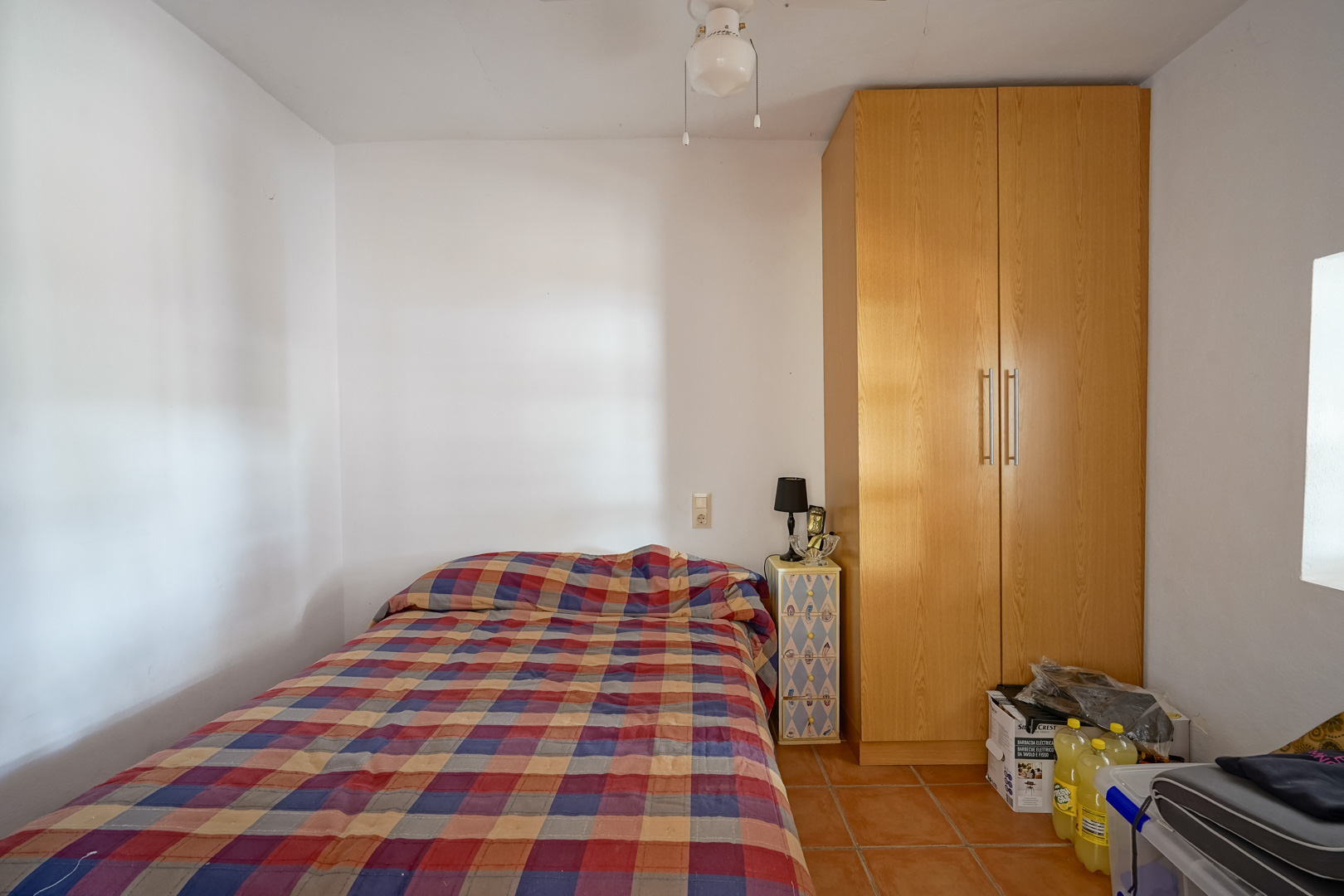 Chambre fonctionnelle avec sol en terre cuite, armoire en bois toute hauteur et murs blancs optimisant la luminosité naturelle.