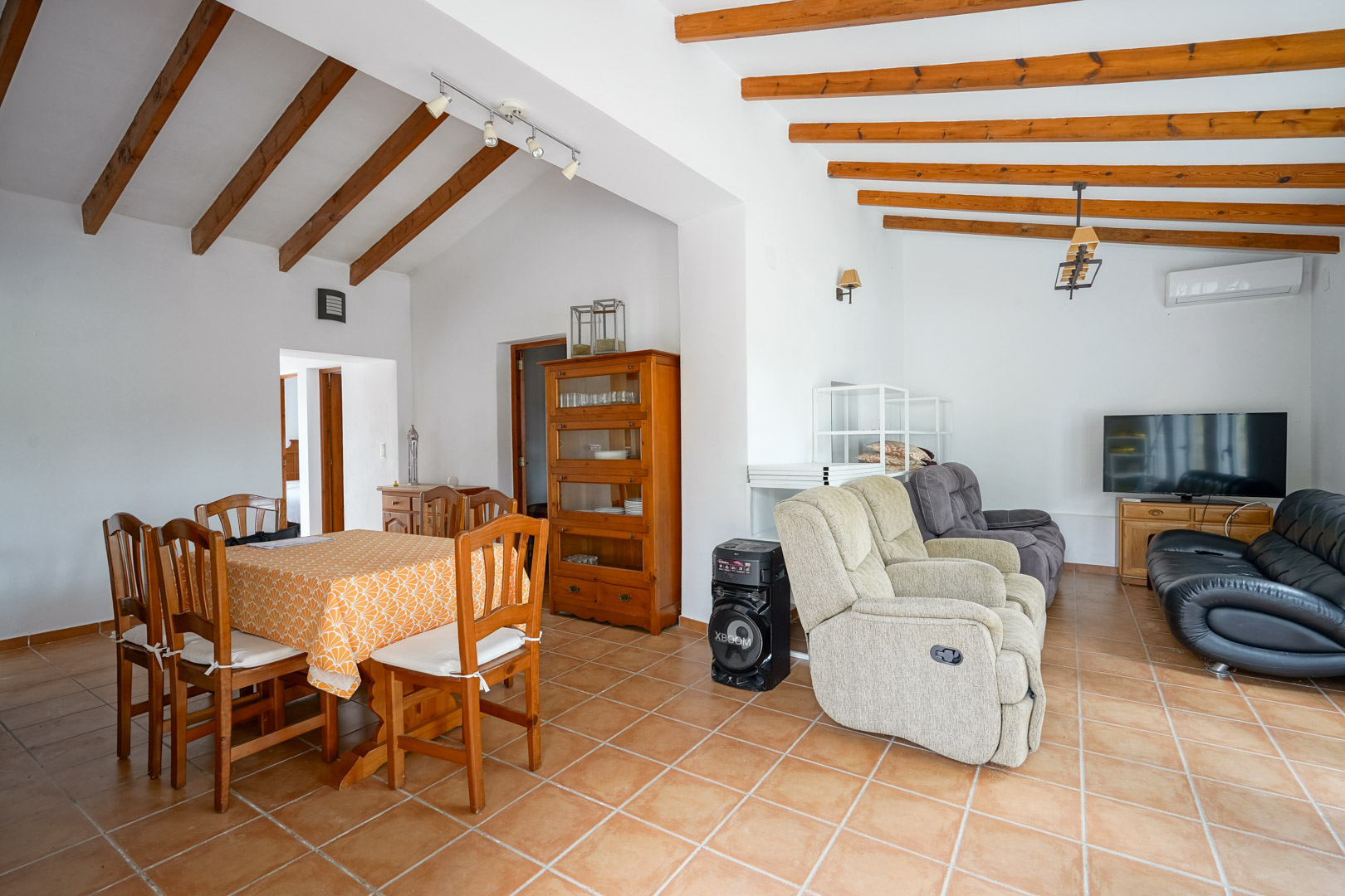 Espace de vie ouvert comprenant un salon et une salle à manger avec poutres apparentes, sol en grès rustique et mobilier en bois traditionnel.
