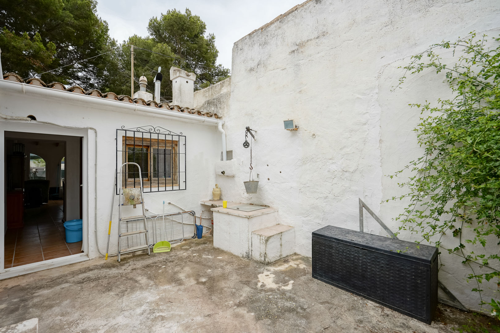 Patio extérieur avec puits traditionnel à poulie, murs blanchis à la chaux et toiture en tuiles canal, entouré d'une pinède.