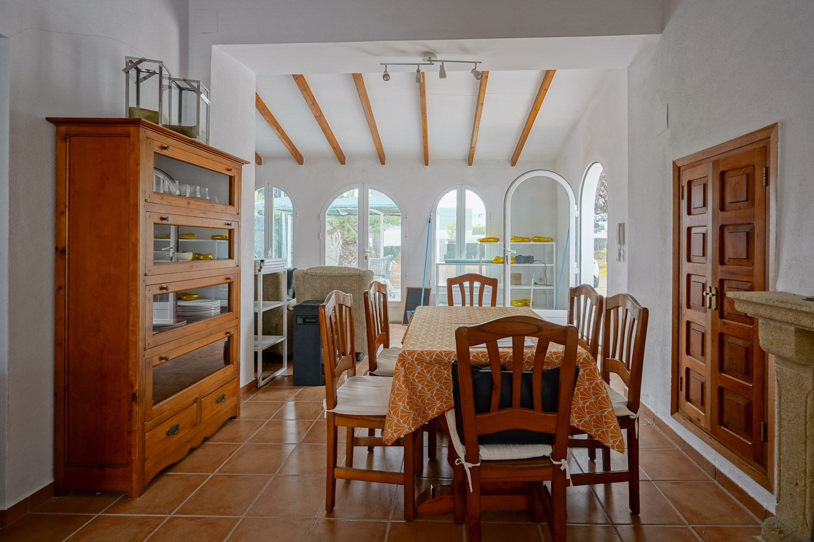 Salle à manger avec poutres en bois apparentes, sol en terre cuite et grandes baies vitrées en arche offrant une luminosité naturelle.