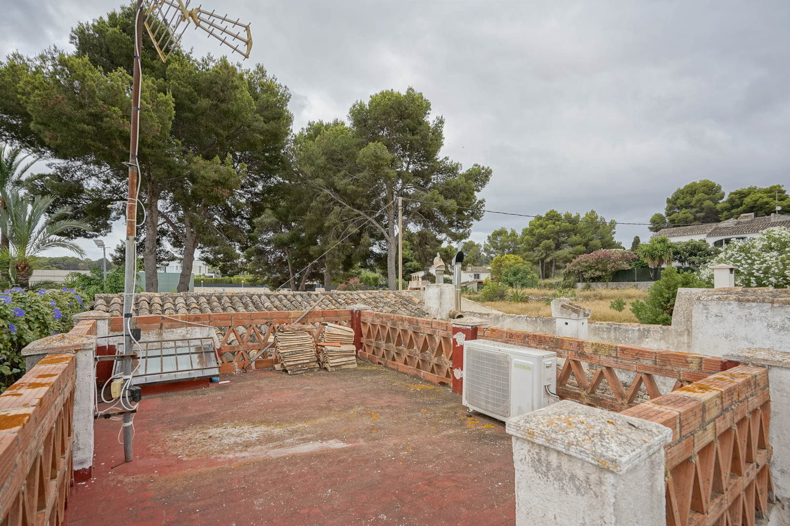 Toit-terrasse avec sol en carrelage rouge et balustrades en briques. L'espace offre une vue sur les pins matures et le quartier résidentiel environnant.