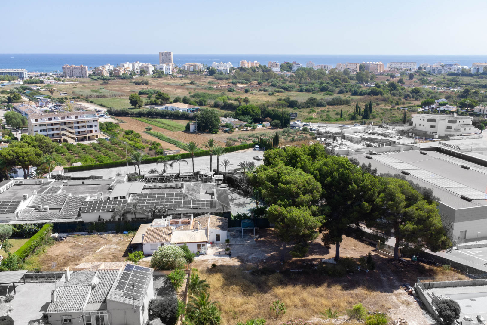 Vue aérienne du terrain de 2 600 m² à Jávea, incluant la villa existante, des pins parasols et une vue dégagée vers la mer Méditerranée.