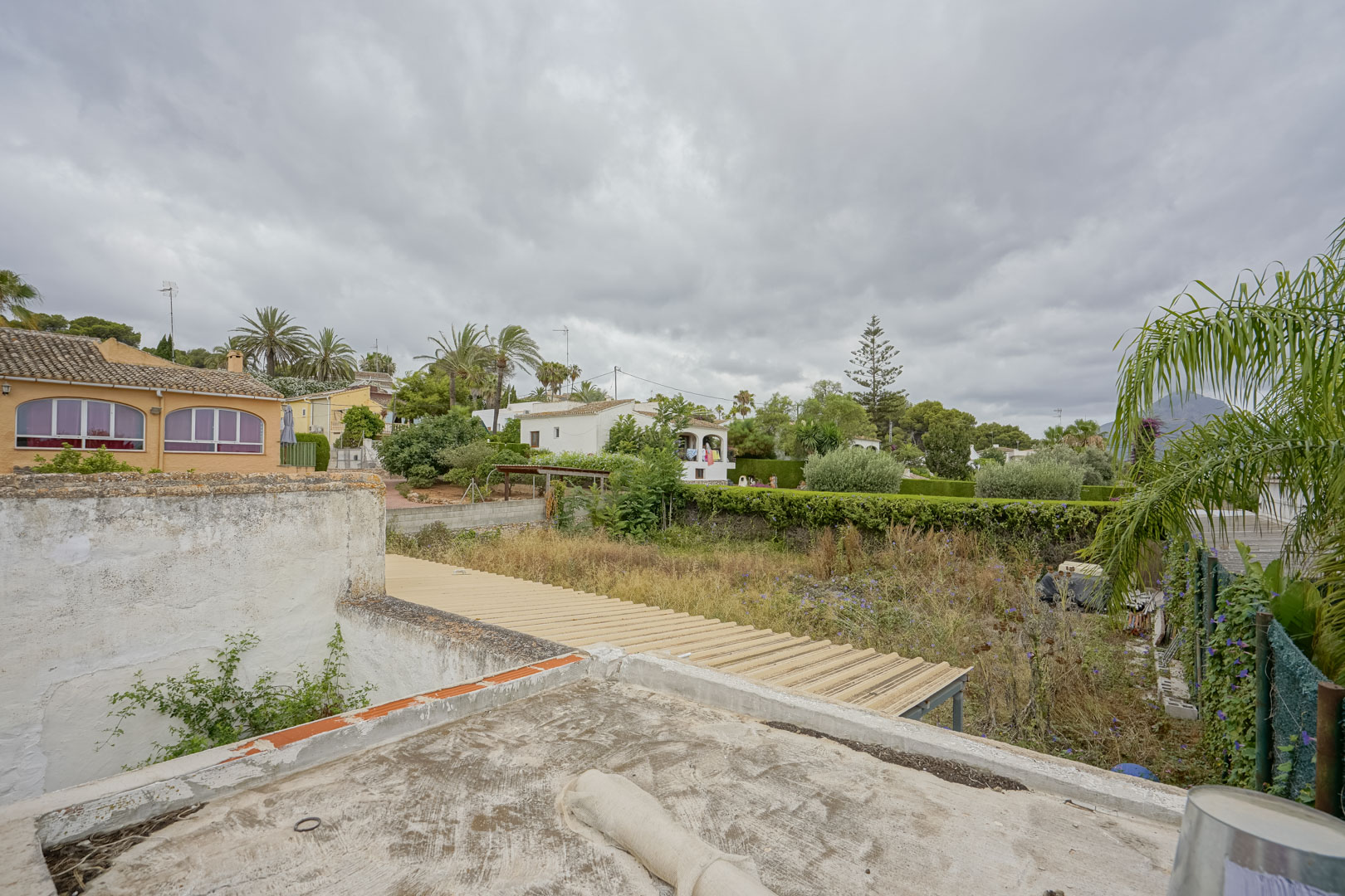 Vue en hauteur du terrain de 2 600 m² révélant son étendue et sa végétation, entouré de villas de quartier avec le massif du Montgó à l'horizon.