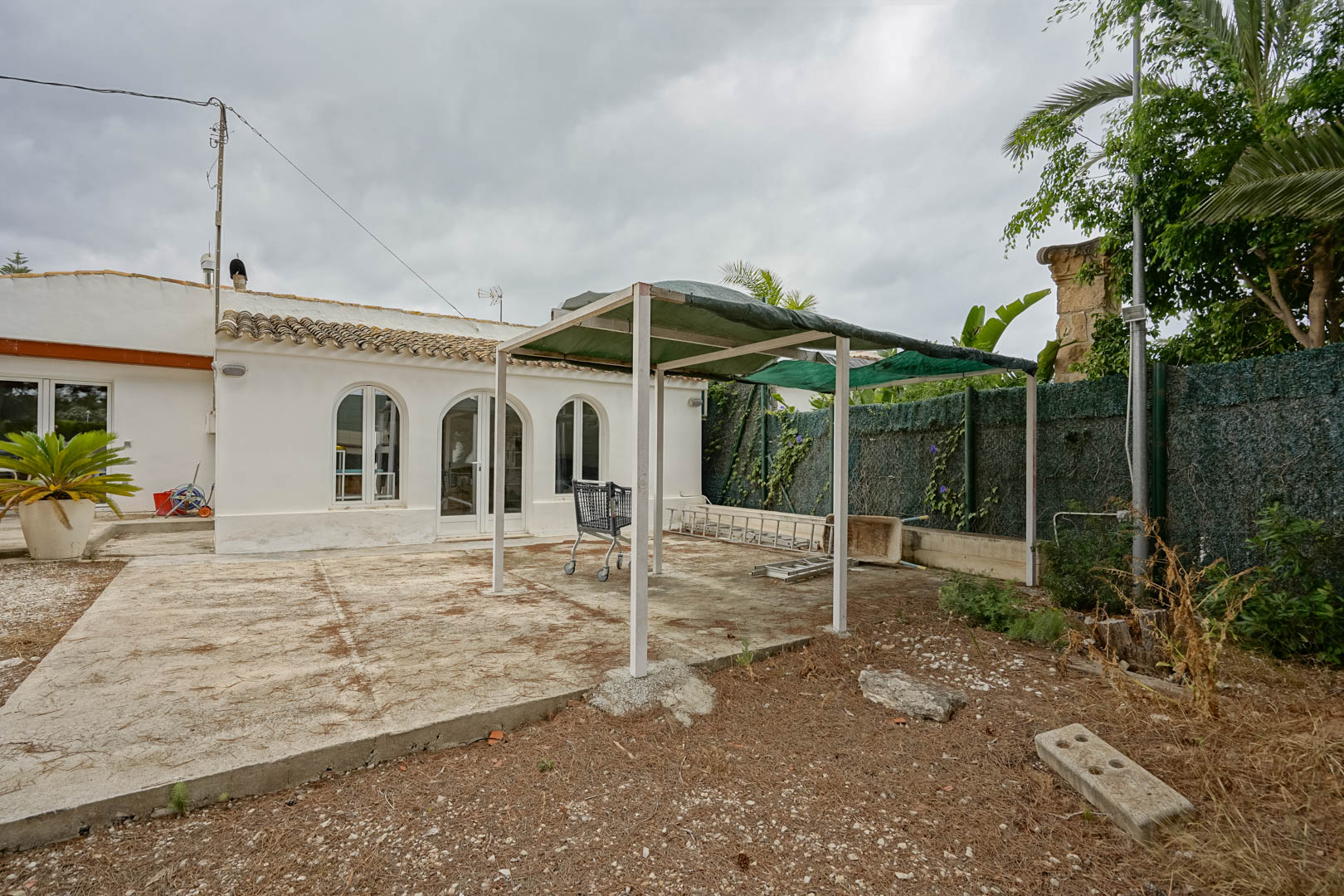 Vue extérieure de la maison actuelle avec façade blanche, fenêtres en arc et une terrasse en béton équipée d'une structure de pergola temporaire.
