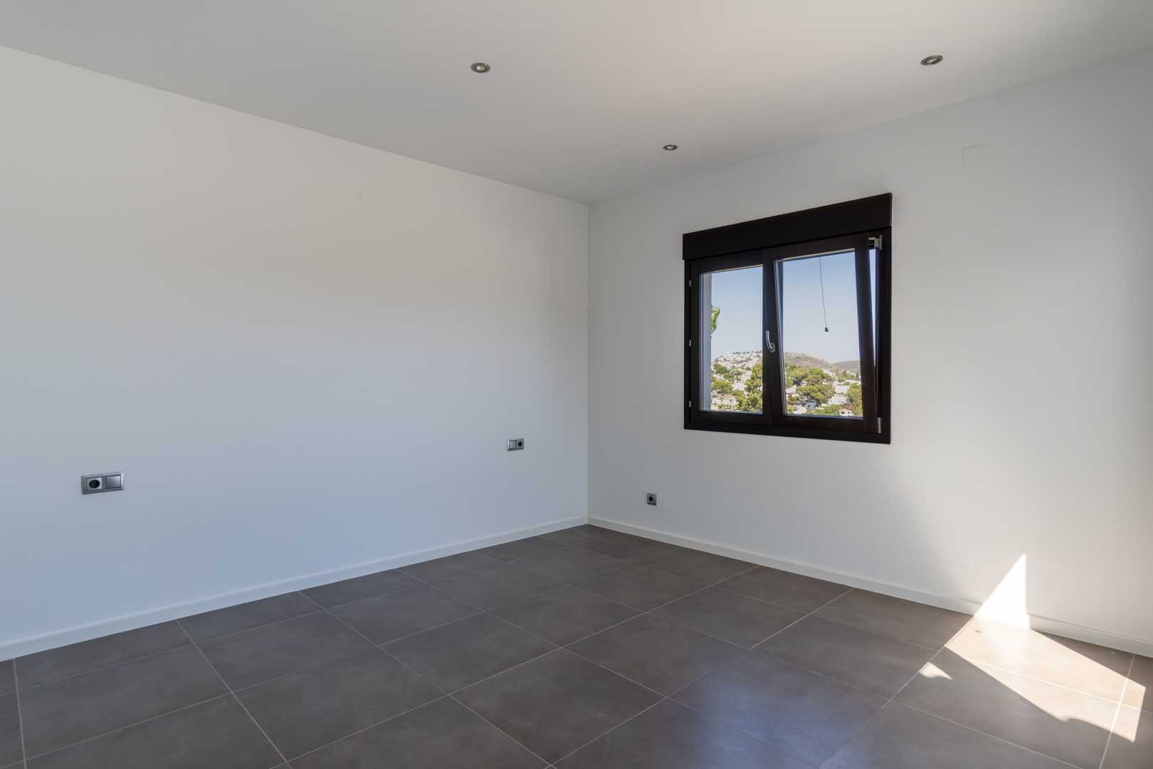 Chambre minimaliste avec sol en grès cérame gris, éclairage LED encastré et fenêtre en aluminium sombre offrant une vue sur le paysage.