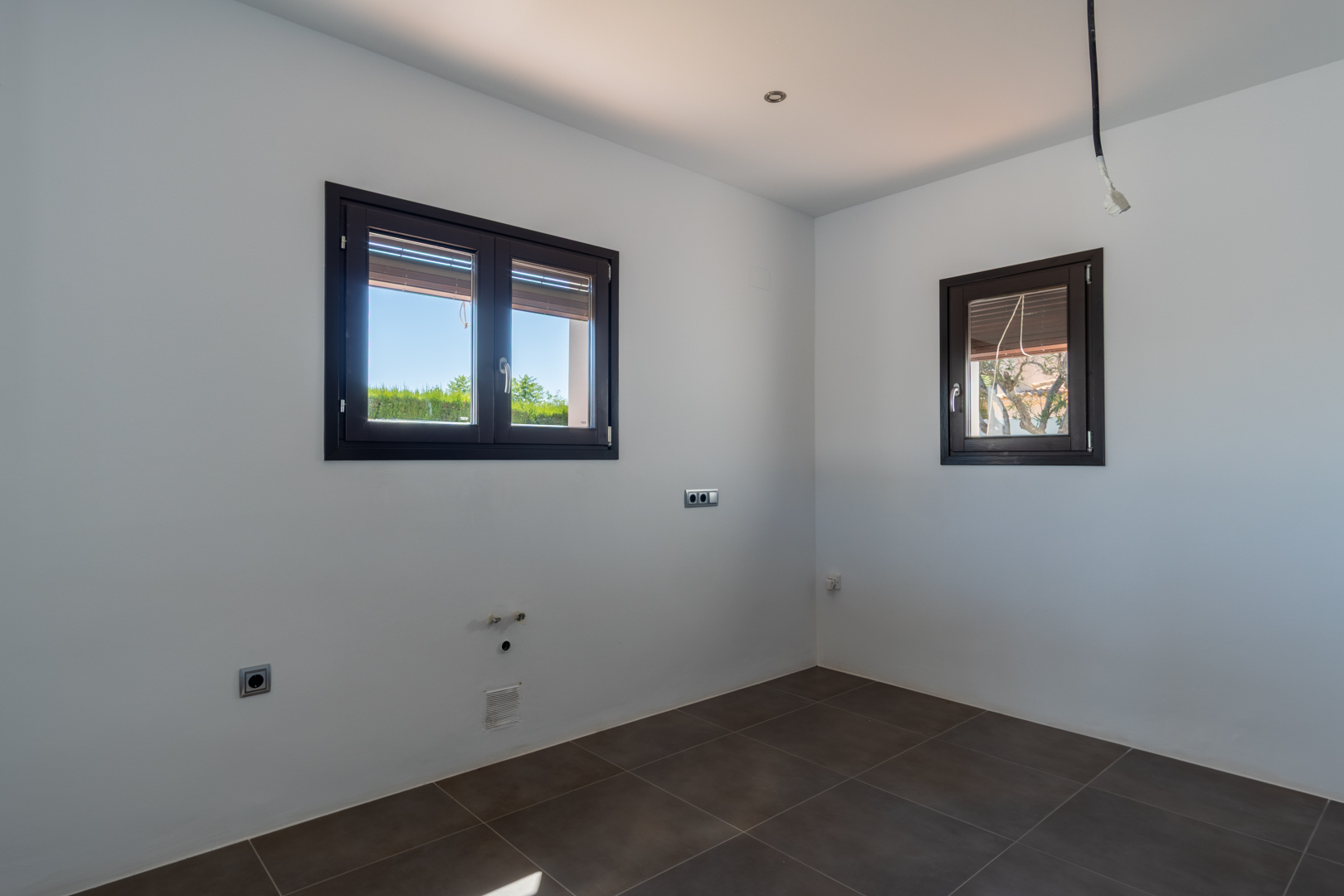 Espace prêt pour l'installation d'une cuisine avec sol en grès cérame, fenêtres en aluminium imitation bois et pré-installations techniques apparentes.