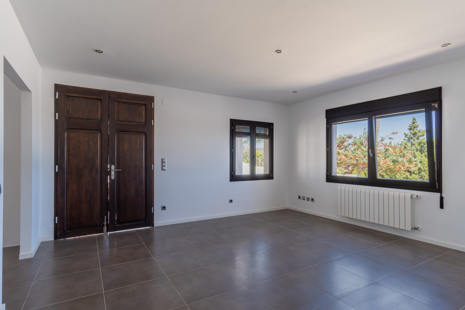 Pièce avec porte ancienne en bois restaurée, fenêtres en aluminium imitation bois, chauffage par radiateur et sol en grès cérame gris.