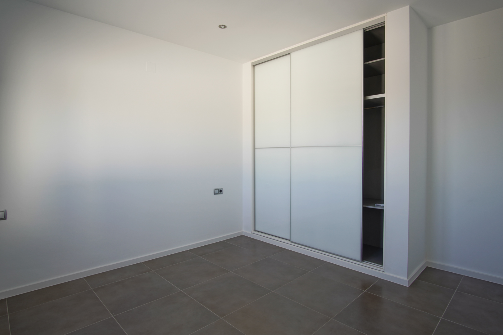 Placard encastré avec portes coulissantes blanches et étagères intérieures, installé dans une pièce épurée avec sol en grès cérame gris.