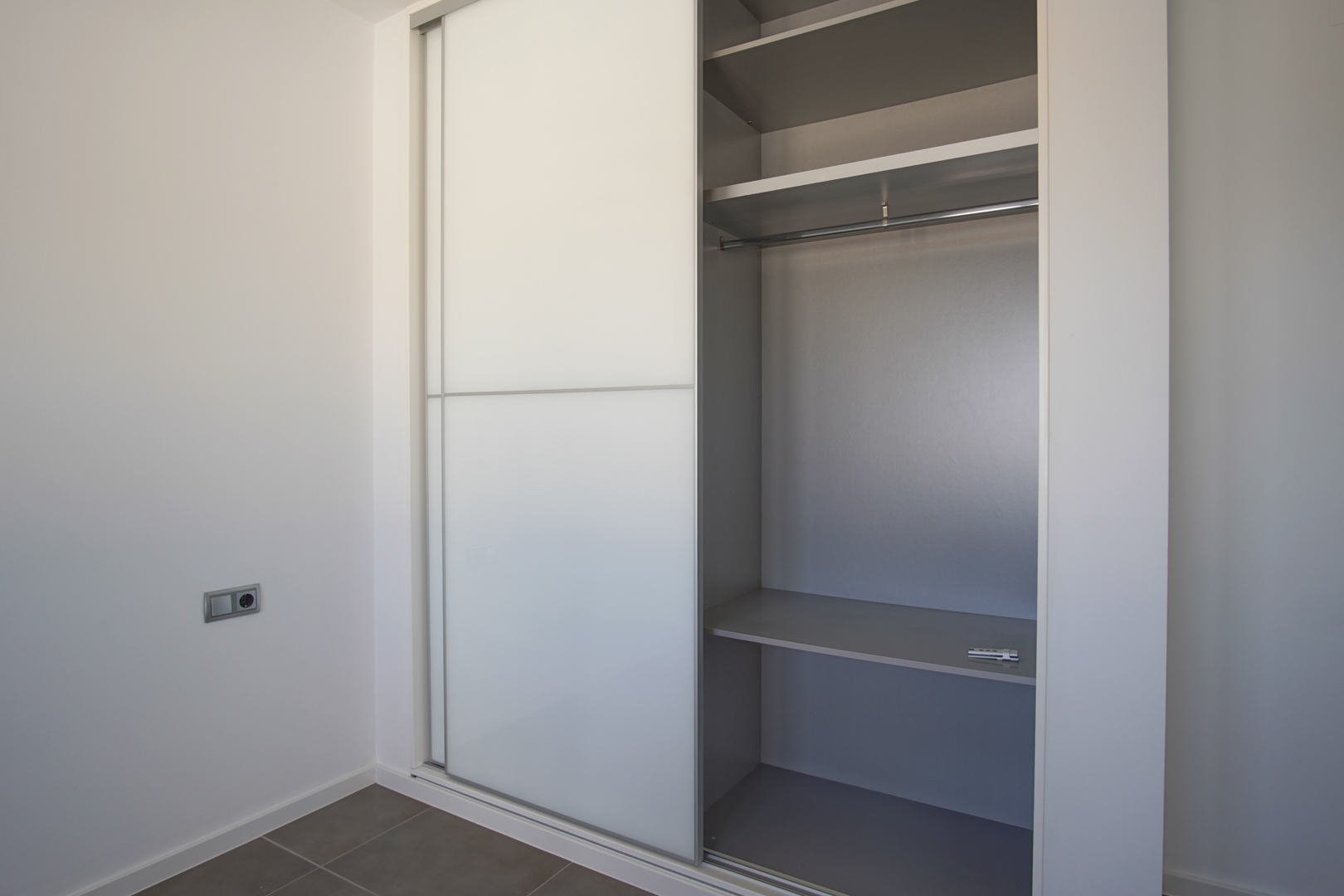 Placard encastré avec portes coulissantes blanches et intérieur gris, comprenant des étagères et une penderie dans une pièce au style épuré.
