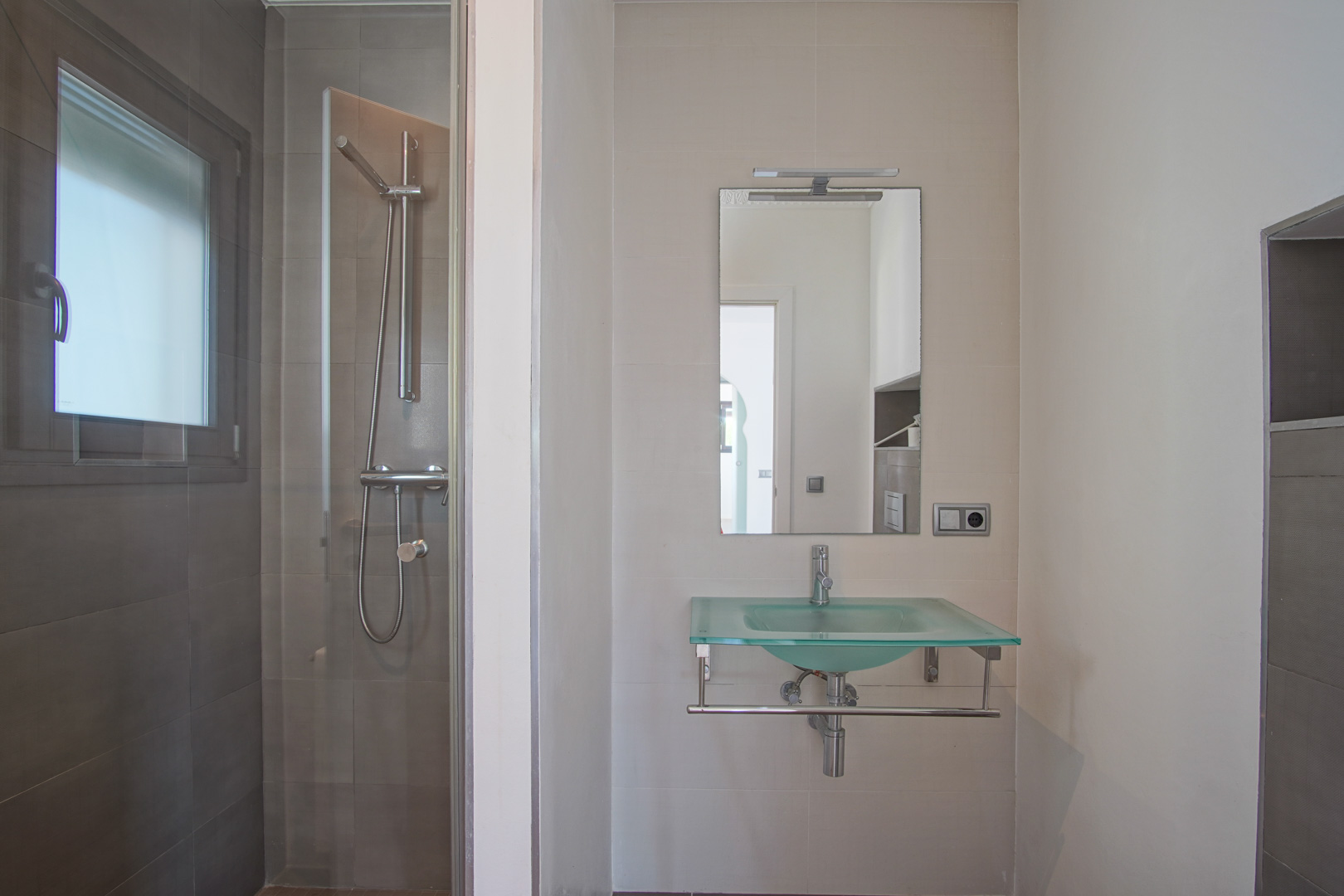 Salle de bain moderne avec une vasque en verre translucide, un miroir éclairé et une douche à l'italienne aux parois gris foncé et paroi vitrée.