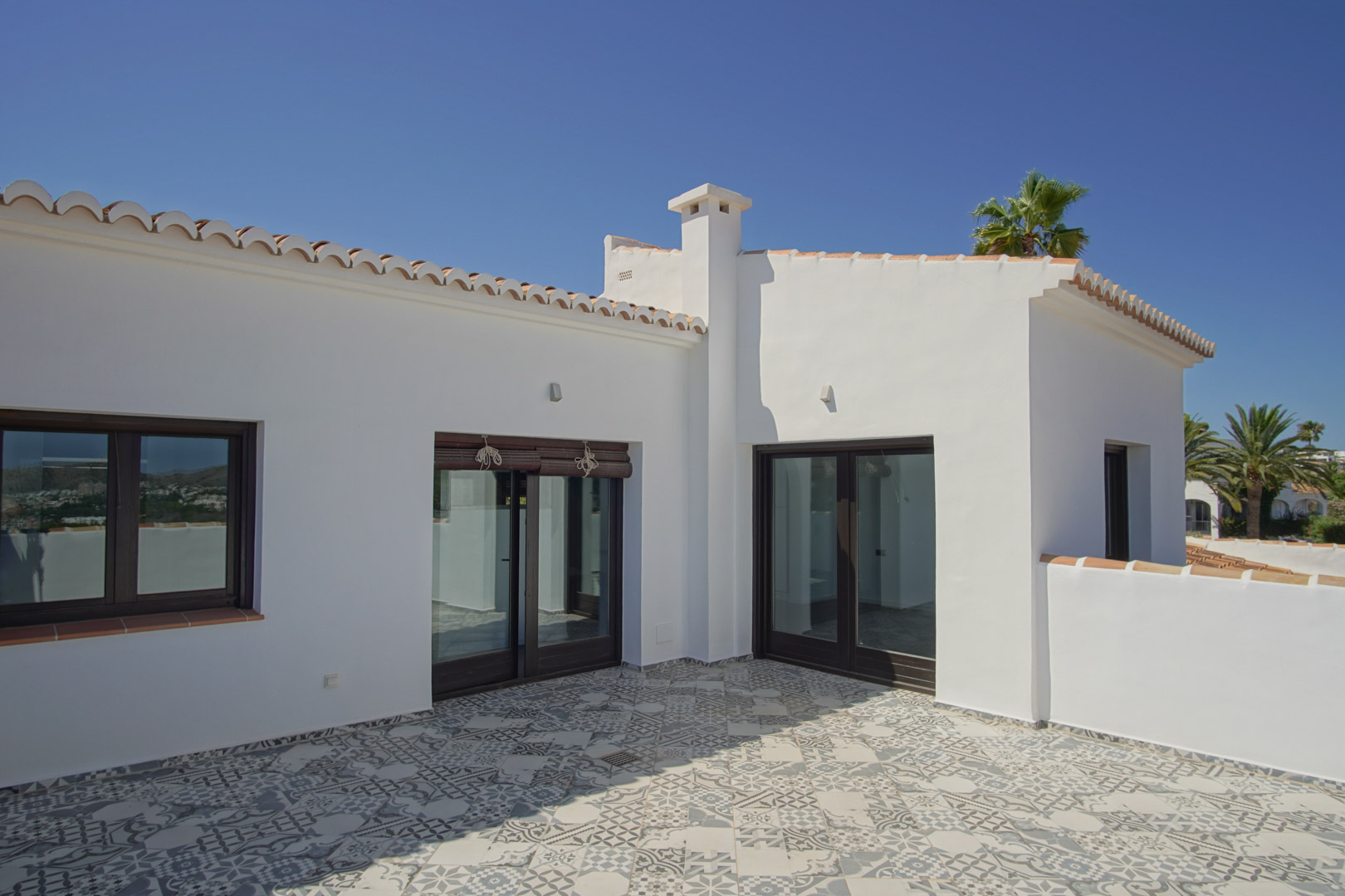 Terrasse solarium avec carrelage à motifs géométriques, menuiseries en aluminium imitation bois et architecture méditerranéenne aux murs blancs.
