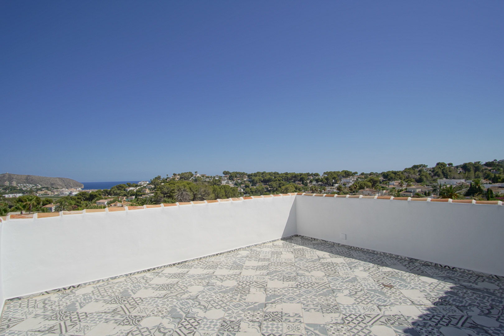 Terrasse solarium avec carrelage à motifs géométriques offrant une vue panoramique sur la mer Méditerranée, la côte de Moraira et les collines environnantes.