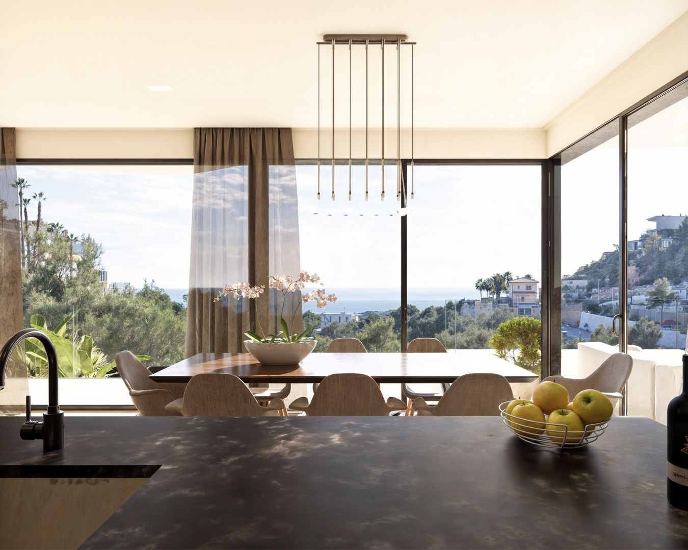 Espace salle à manger avec table en bois et luminaire design, ouvert sur de larges baies vitrées offrant une vue panoramique sur la mer Méditerranée.