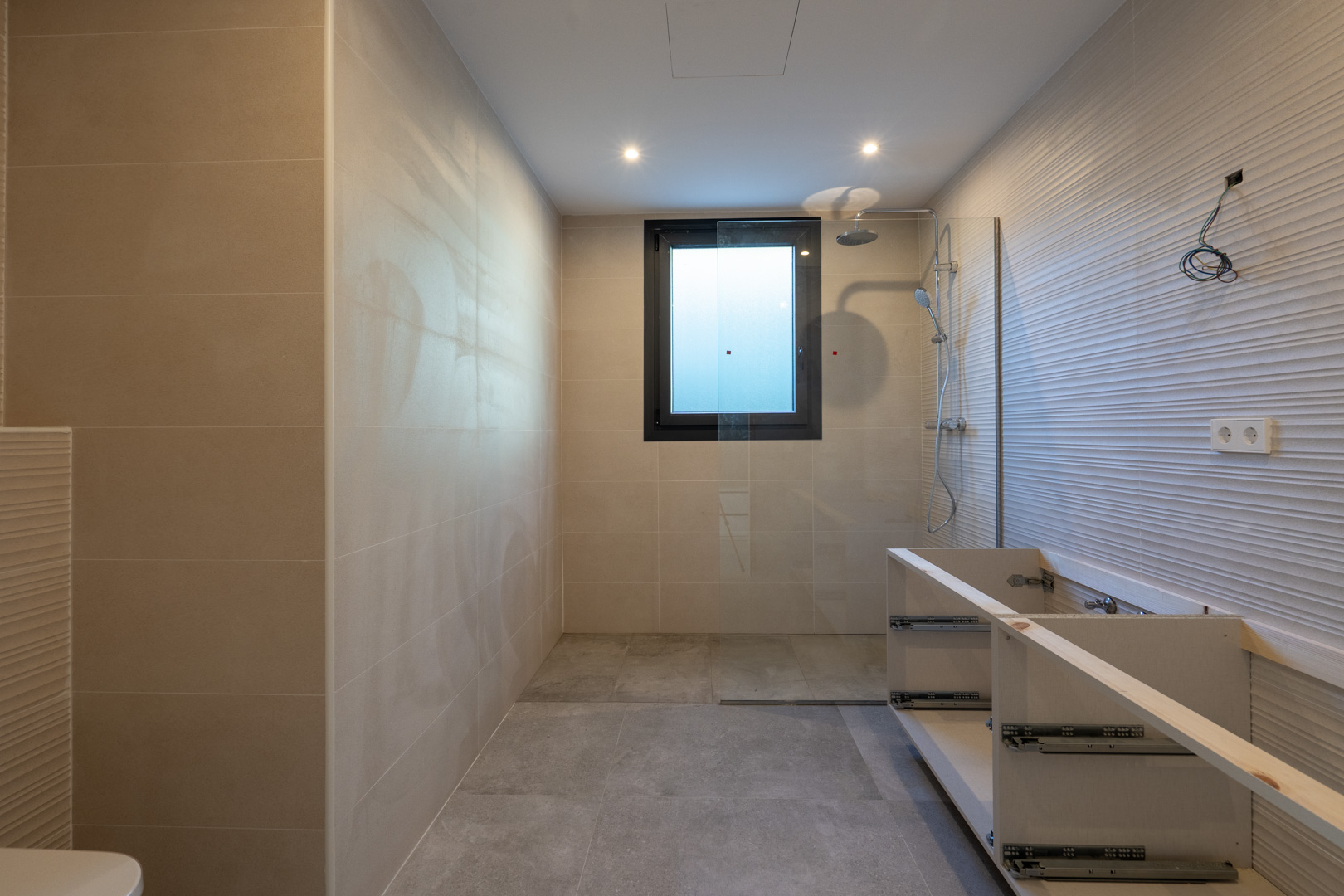 Détail d'une salle de bain moderne avec douche, fenêtre carrée et meuble-lavabo non fini.