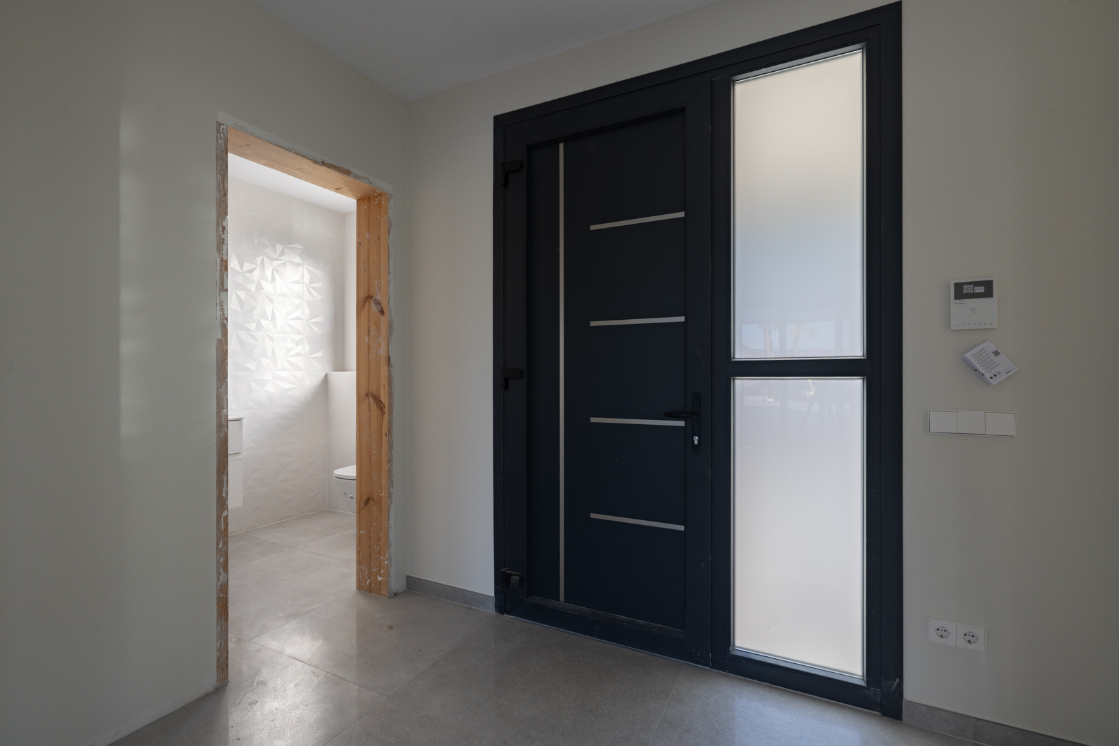 Entrée moderne avec porte design et accès à des toilettes avec mur en carreaux texturés.