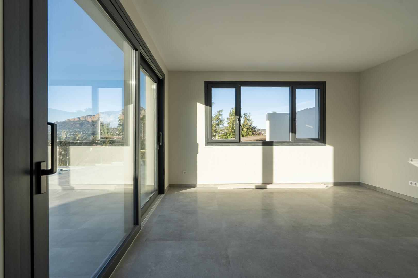 Espace intérieur lumineux avec carrelage gris, larges baies vitrées coulissantes et vues extérieures.