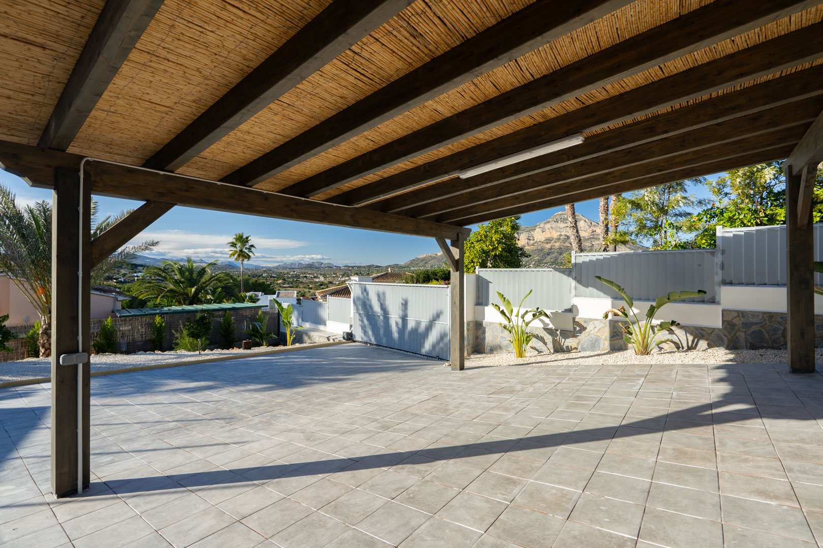 Pergola avec plafond en roseaux et sol carrelé, donnant sur la verdure et les montagnes.