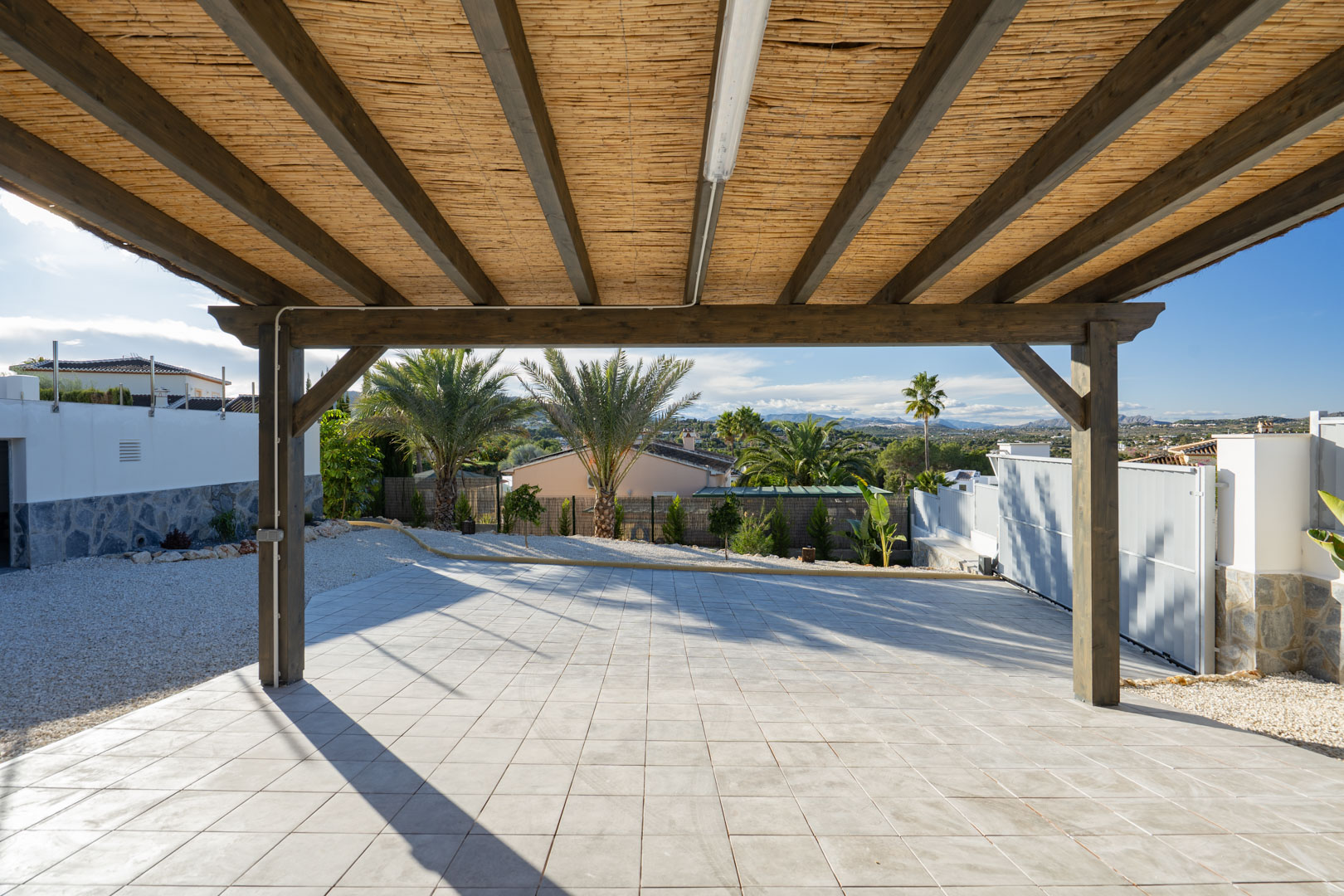 Pergola avec structure en bois et couverture en roseaux, sur sol carrelé dans villa à Jávea.
