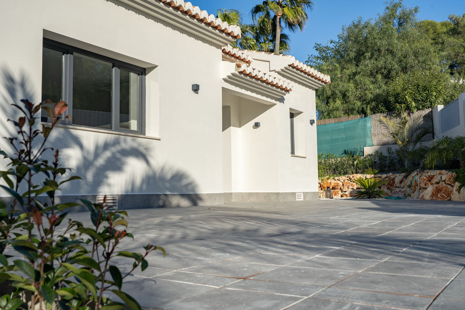 Vue extérieure de la villa avec une façade blanche, des tuiles en terre cuite et un sol carrelé gris.