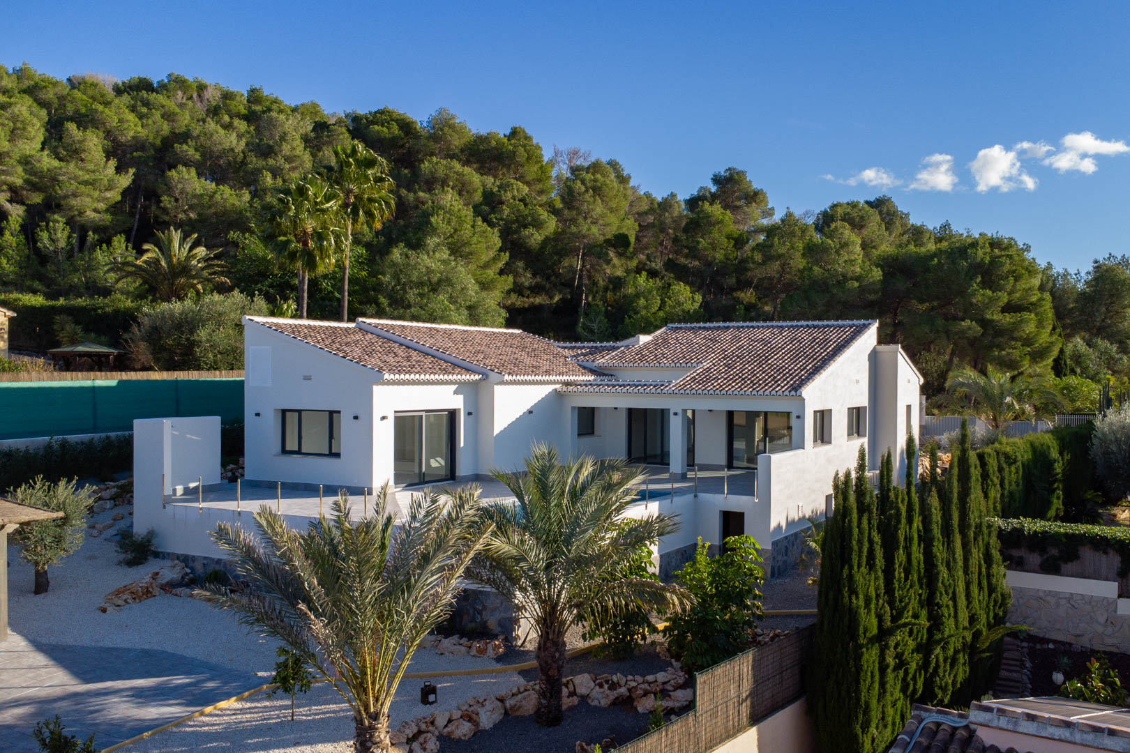 Vue extérieure de la villa neuve à Jávea, soulignant son design moderne et sa piscine privée entourée de verdure luxuriante.