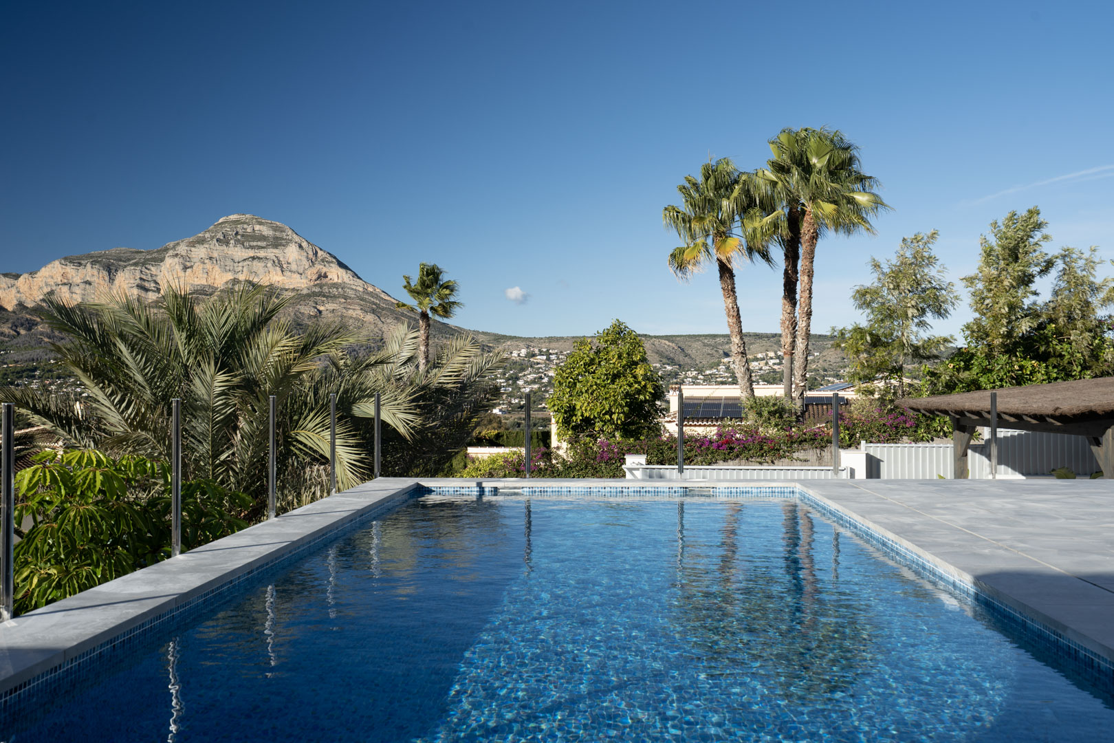 Vue sur la piscine privée avec des mosaïques bleues, entourée de verdure et avec une montagne majestueuse en arrière-plan.