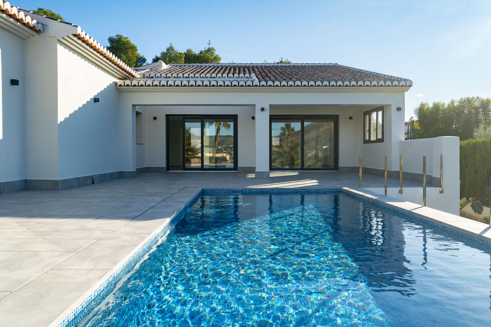 Vue sur la piscine privée avec mosaïque bleue et la terrasse carrelée grise de la villa.