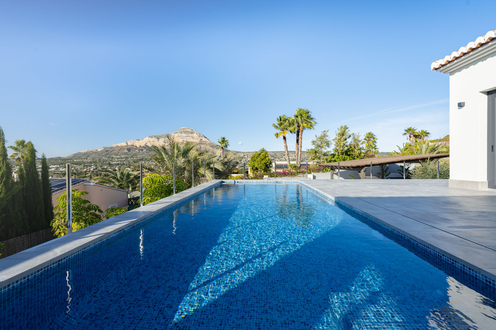 Vue sur la piscine privée avec mosaïque bleue, terrasse carrelée grise et vue sur la montagne à Jávea.