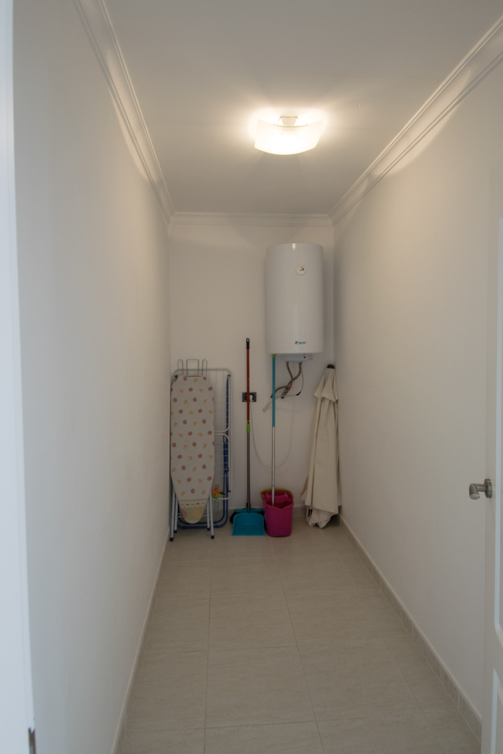 Buanderie fonctionnelle équipée d'un chauffe-eau électrique, d'un espace de rangement pour le matériel de nettoyage et d'un sol en grès.