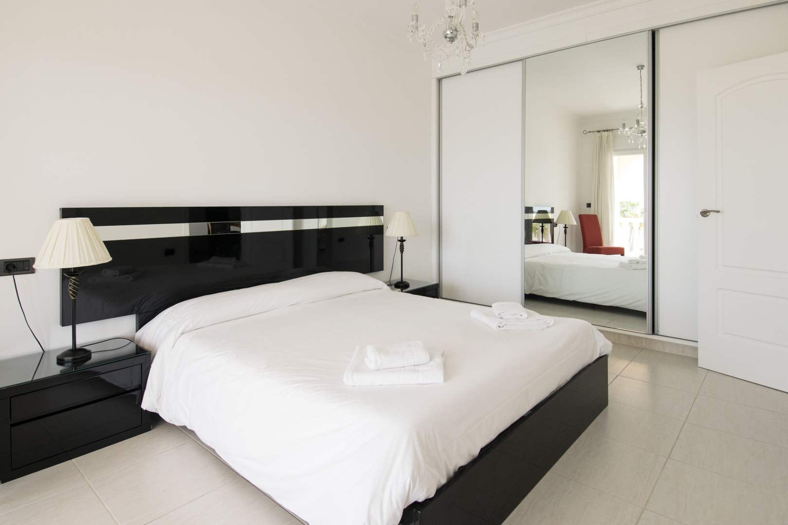 Chambre principale avec lit double, tête de lit laquée noire, tables de chevet assorties et un grand placard intégré avec portes coulissantes en miroir.