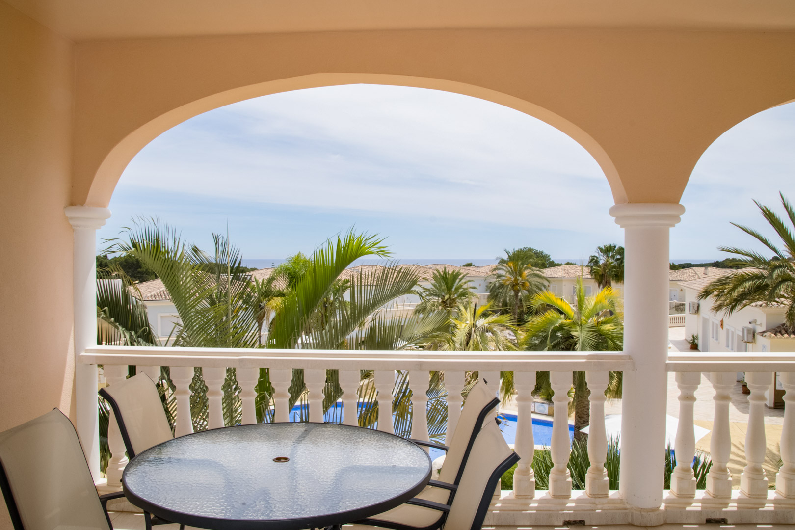 Terrasse couverte avec arcades et balustrade en pierre, offrant un coin repas extérieur. Vue dégagée sur les jardins tropicaux, la piscine lagon et l'horizon marin.