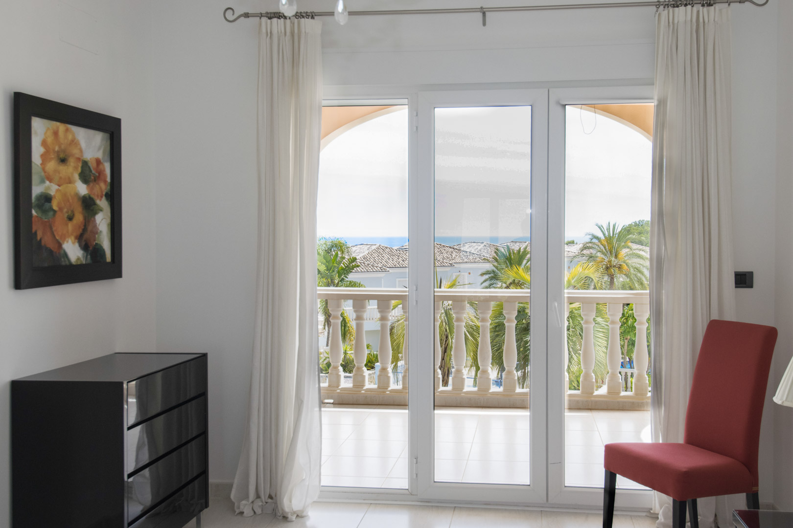 Vue intérieure s'ouvrant sur une terrasse couverte avec balustrades en pierre, offrant une perspective sur les jardins tropicaux et la mer à l'horizon.
