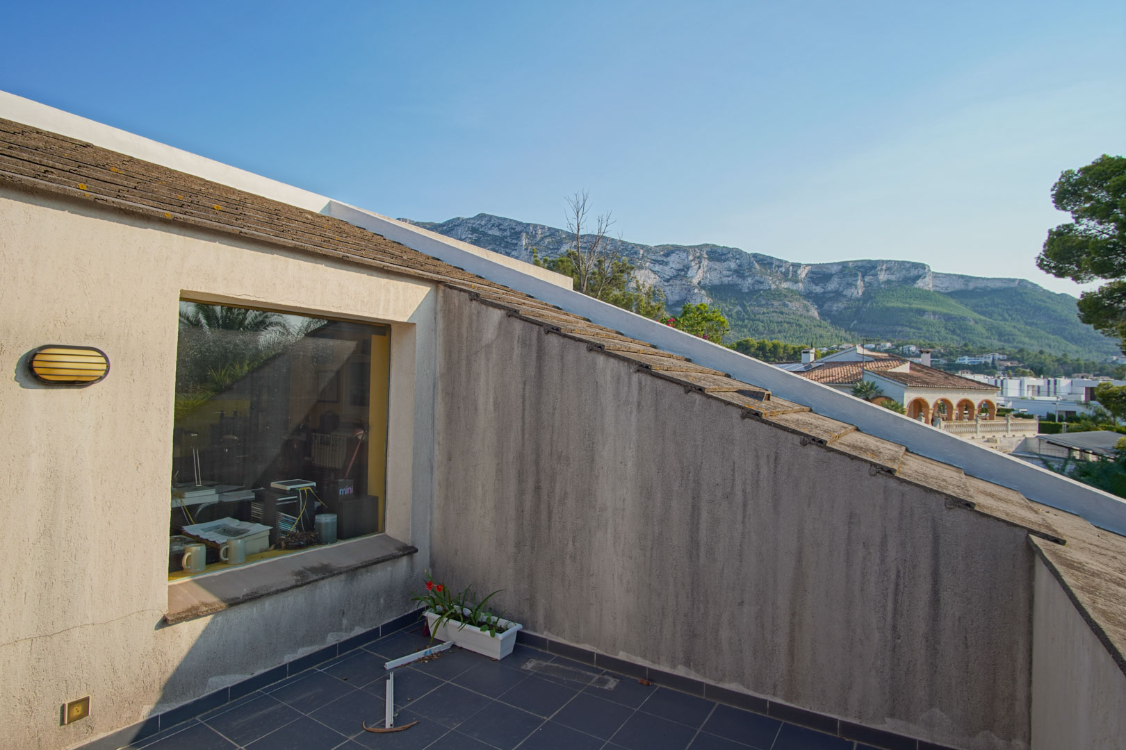 Balcon à l'étage supérieur avec carrelage sombre offrant une vue sur le Montgó. Une grande fenêtre donne un aperçu de l'espace bureau intérieur.