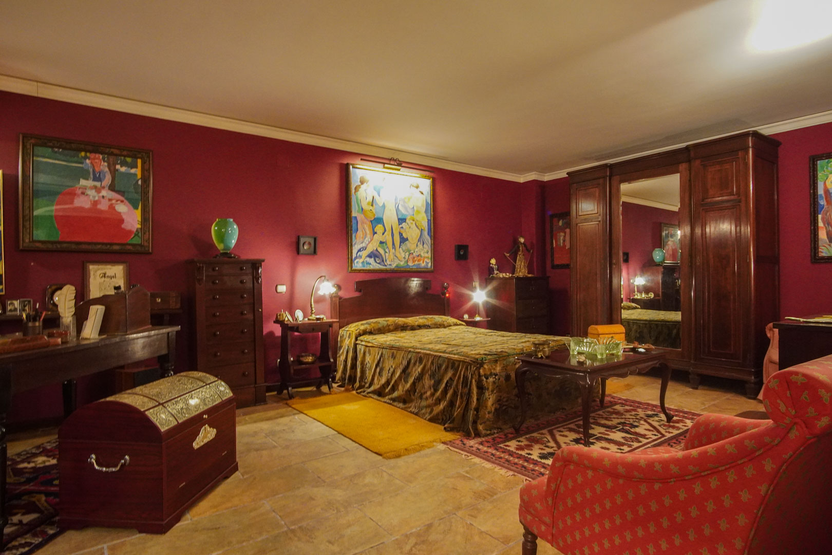 Chambre de style classique avec murs bordeaux, mobilier en bois massif, sol en pierre naturelle et une grande armoire avec miroir central.