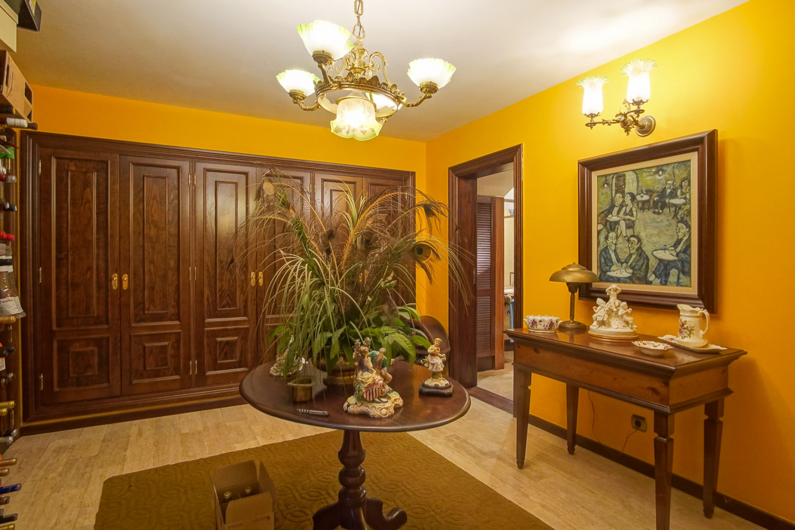 Hall d'entrée avec murs jaune moutarde, placards en bois sombre, sol en marbre et mobilier classique éclairé par des lustres de style traditionnel.