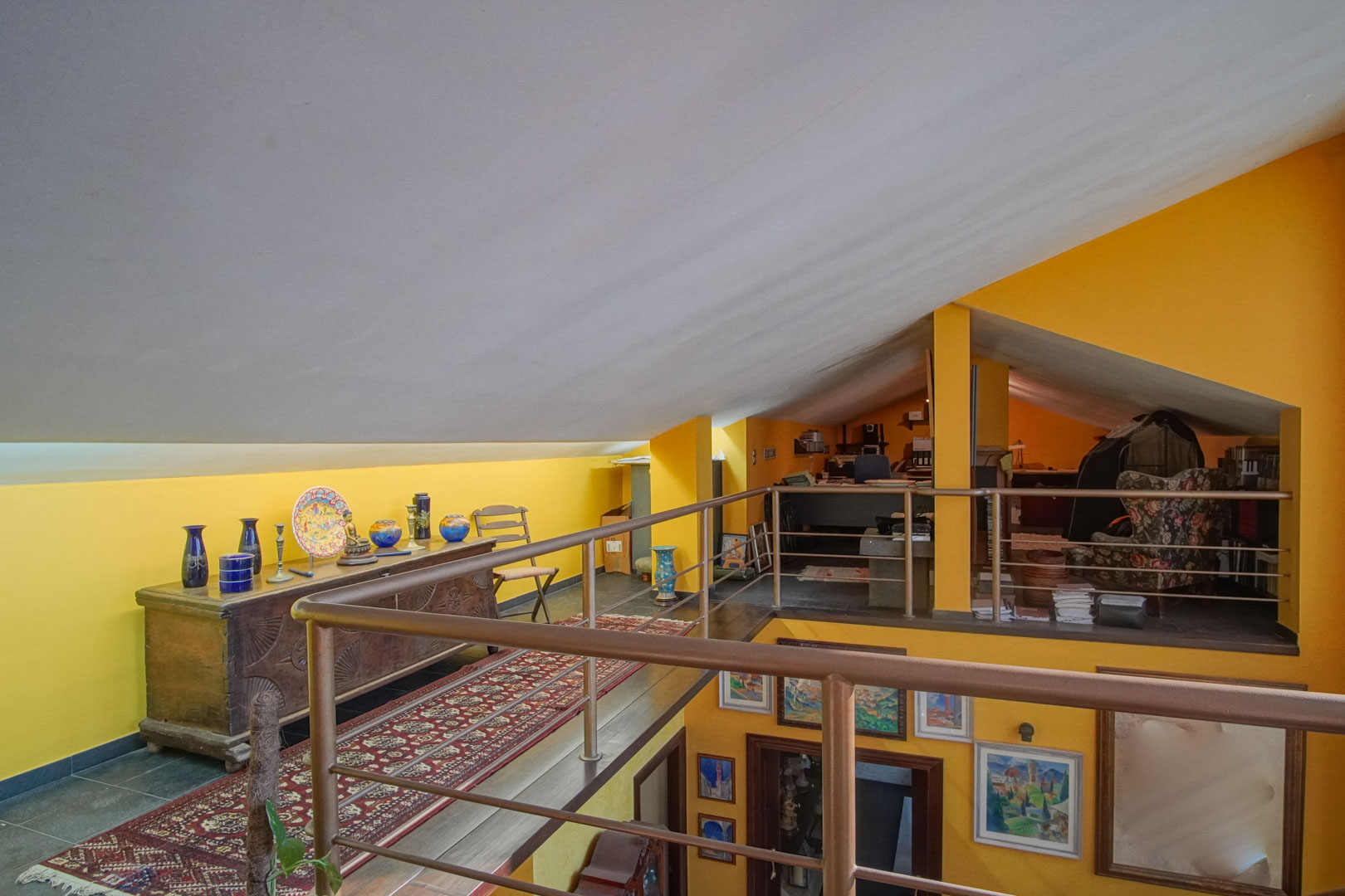 Mezzanine spacieuse sous combles avec murs jaune vif et garde-corps métallique. Cet espace polyvalent dispose d'un mobilier classique et d'une vue plongeante sur le niveau inférieur.