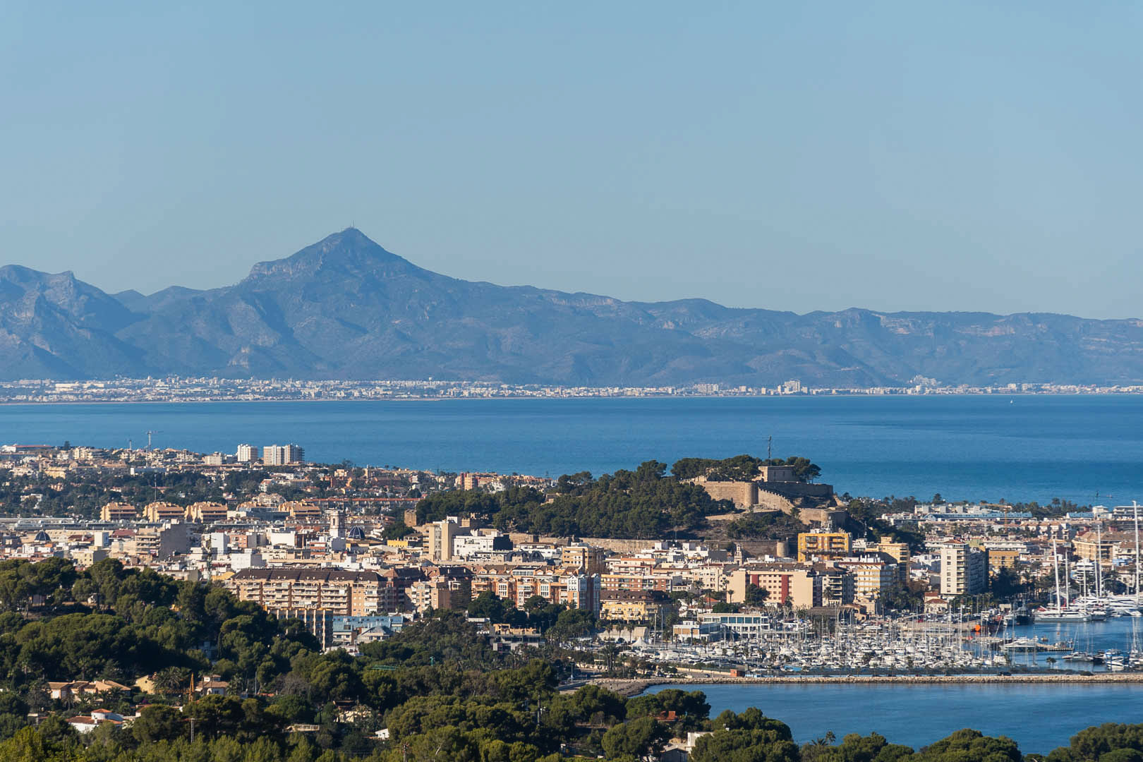 Vue panoramique de Dénia montrant le château historique, le port de plaisance et les montagnes bordant la mer Méditerranée.
