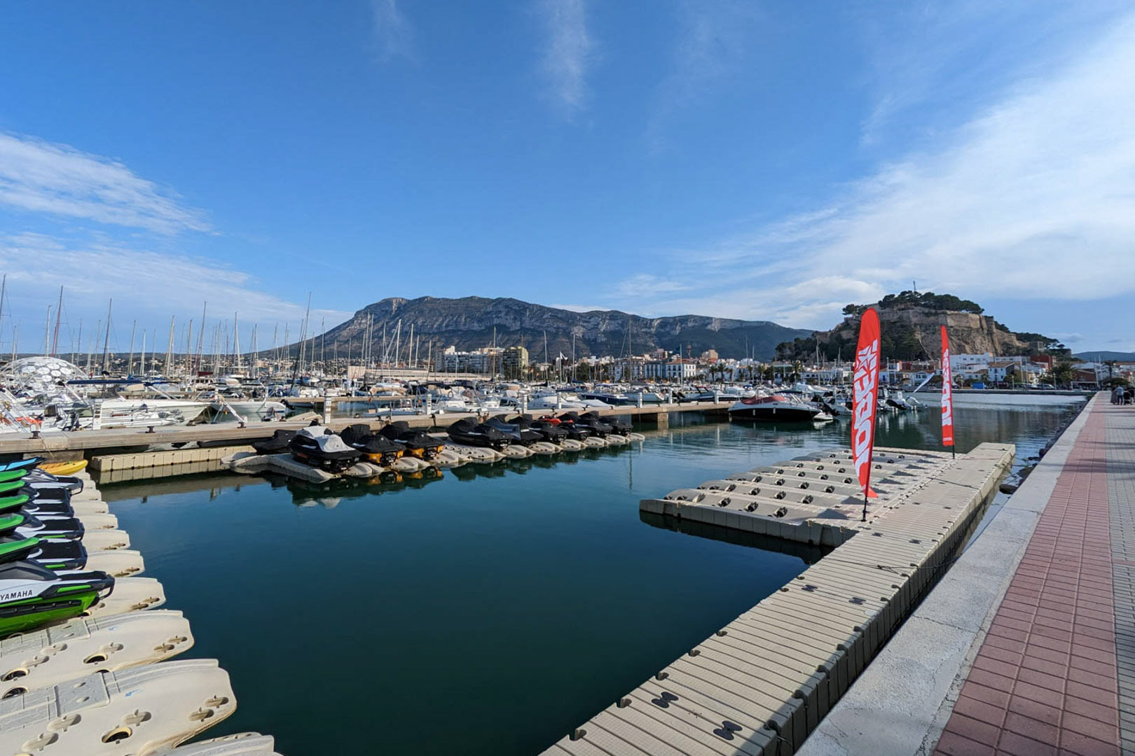 Vue panoramique du port de plaisance de Dénia avec le château historique, le mont Montgó en arrière-plan et les quais pour jet-skis.