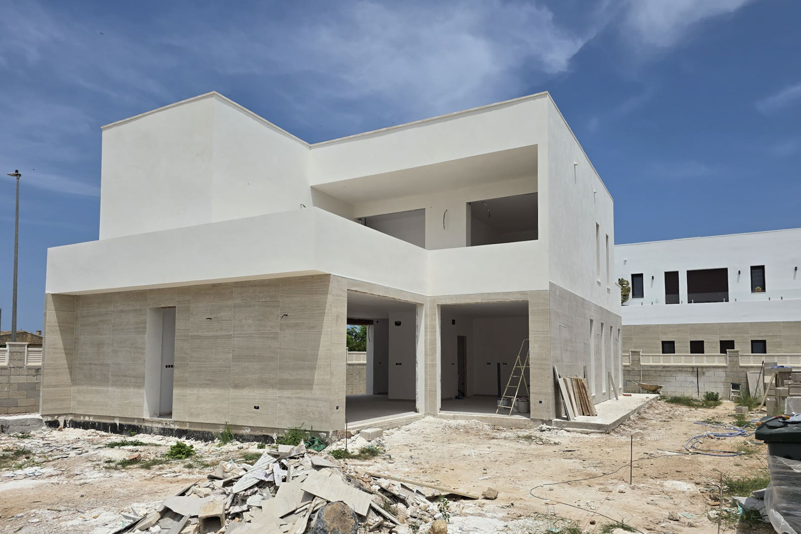 Façade d'une villa moderne en construction avec revêtement en pierre au rez-de-chaussée, volumes blancs géométriques et larges ouvertures pour les futures baies vitrées.