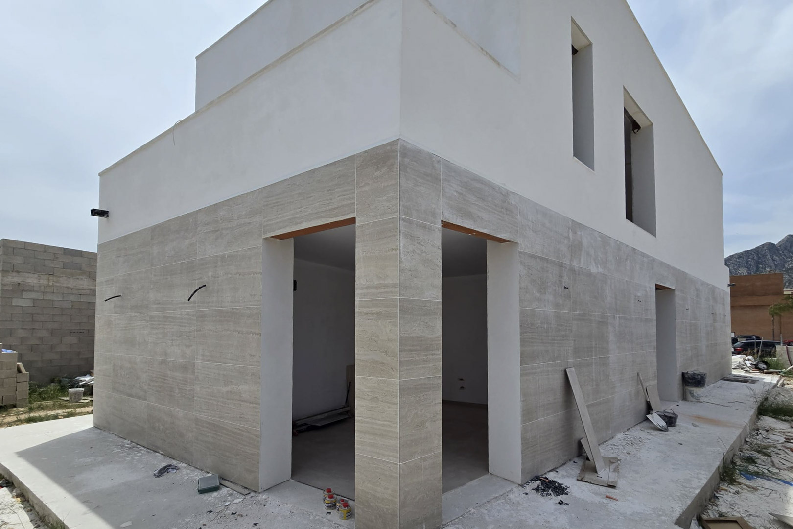 Façade extérieure en construction avec revêtement en pierre au rez-de-chaussée et finitions blanches à l'étage, soulignant des lignes épurées et de larges ouvertures.