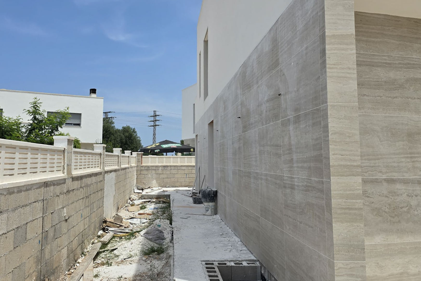 Façade latérale en cours de construction avec un revêtement en pierre de grand format, illustrant les finitions modernes et le mur d'enceinte de la propriété.