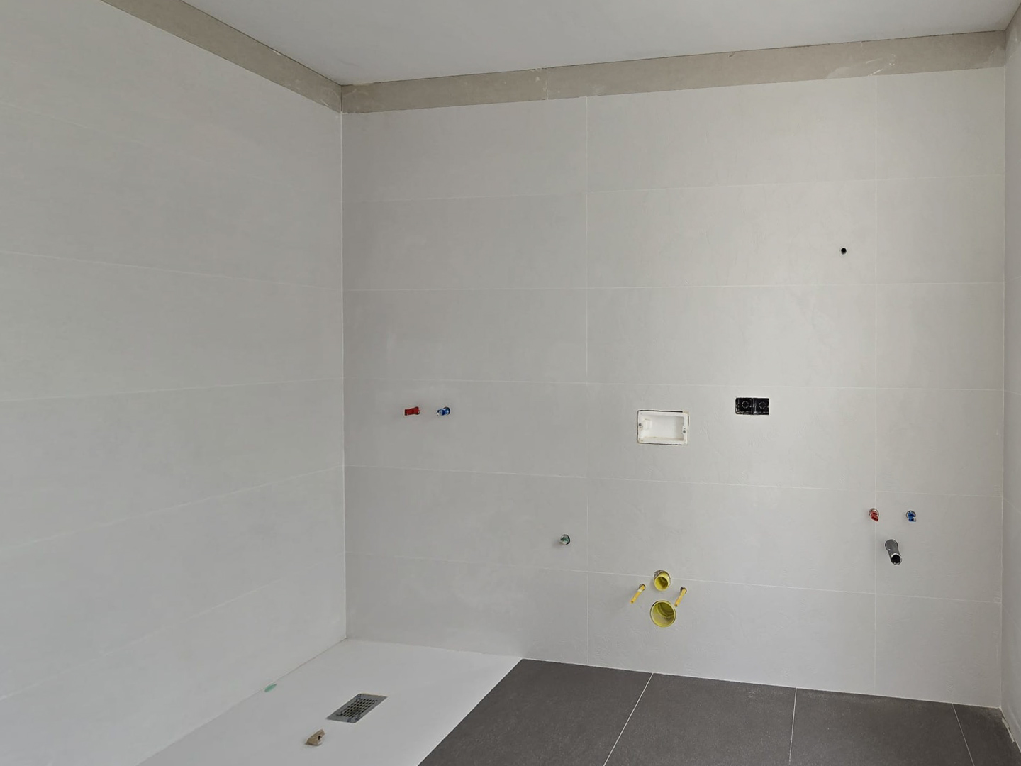 Salle de bain en chantier avec grand carrelage mural blanc, receveur de douche extra-plat et pré-installations techniques pour les futurs équipements sanitaires.