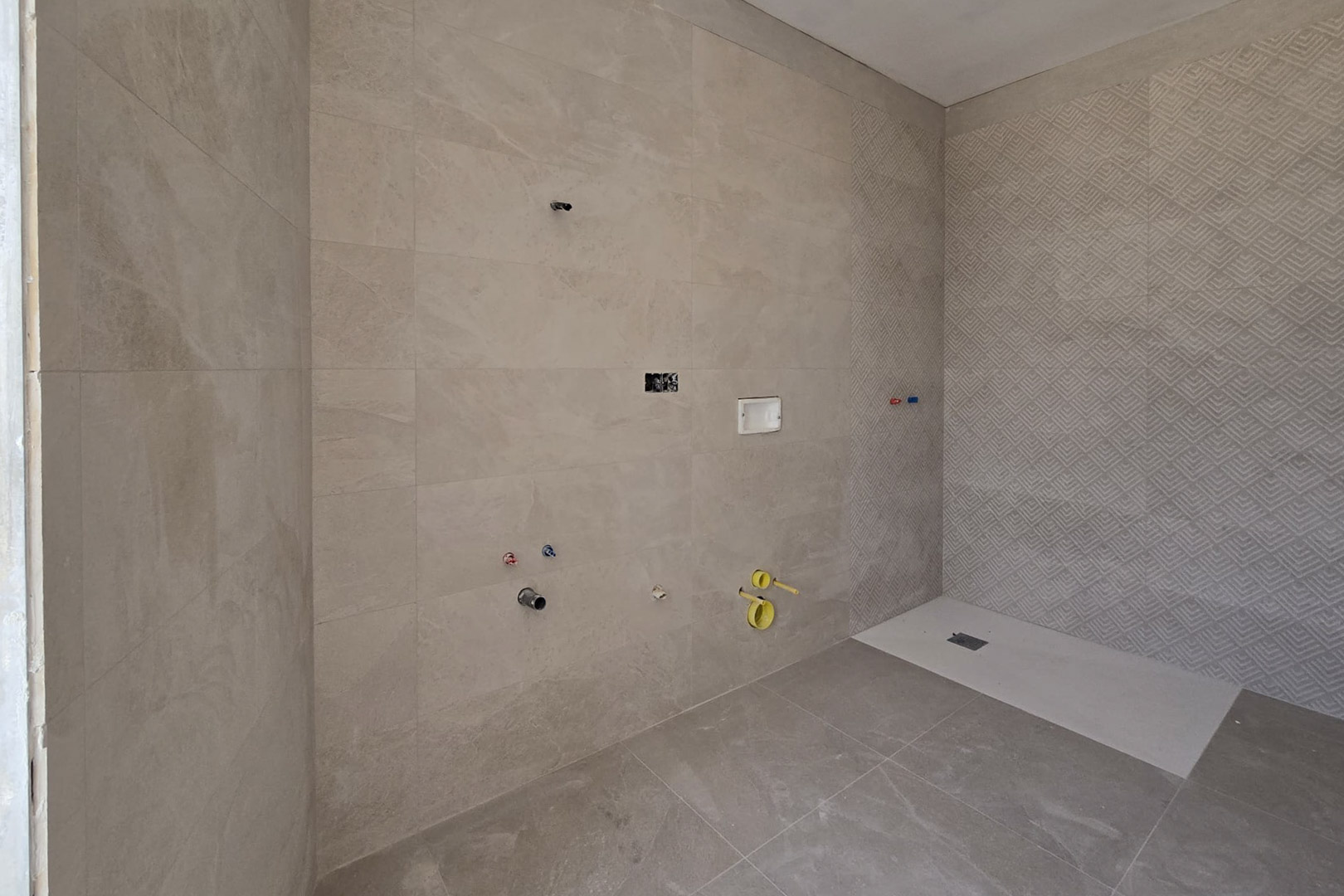 Salle de bain en construction avec carrelage en grès cérame beige, mur de douche à motifs géométriques et receveur de douche extra-plat blanc.