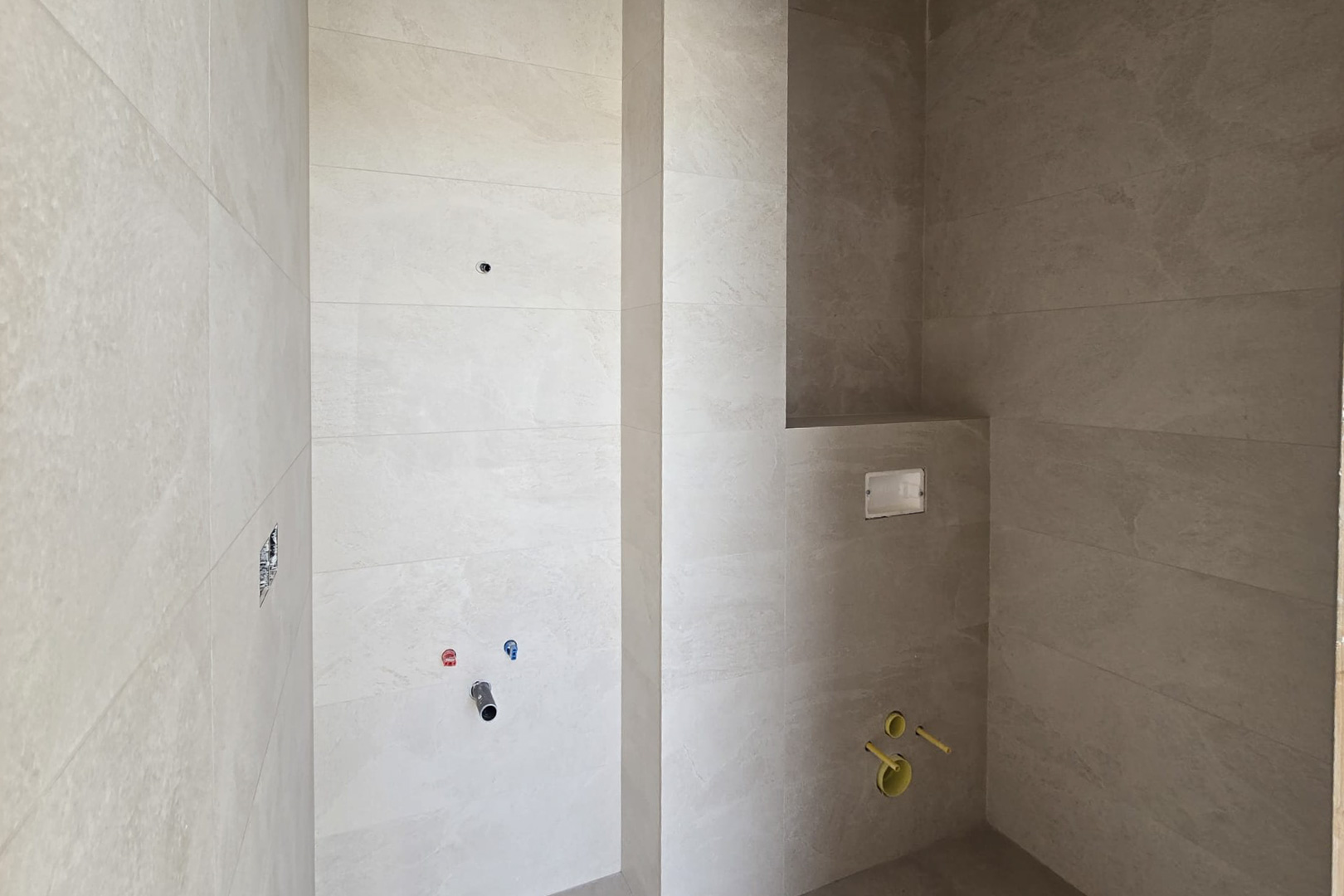 Salle de bain en construction avec carrelage mural en grès cérame beige, raccordements pour vasque et bâti-support pour WC suspendu avec niche intégrée.