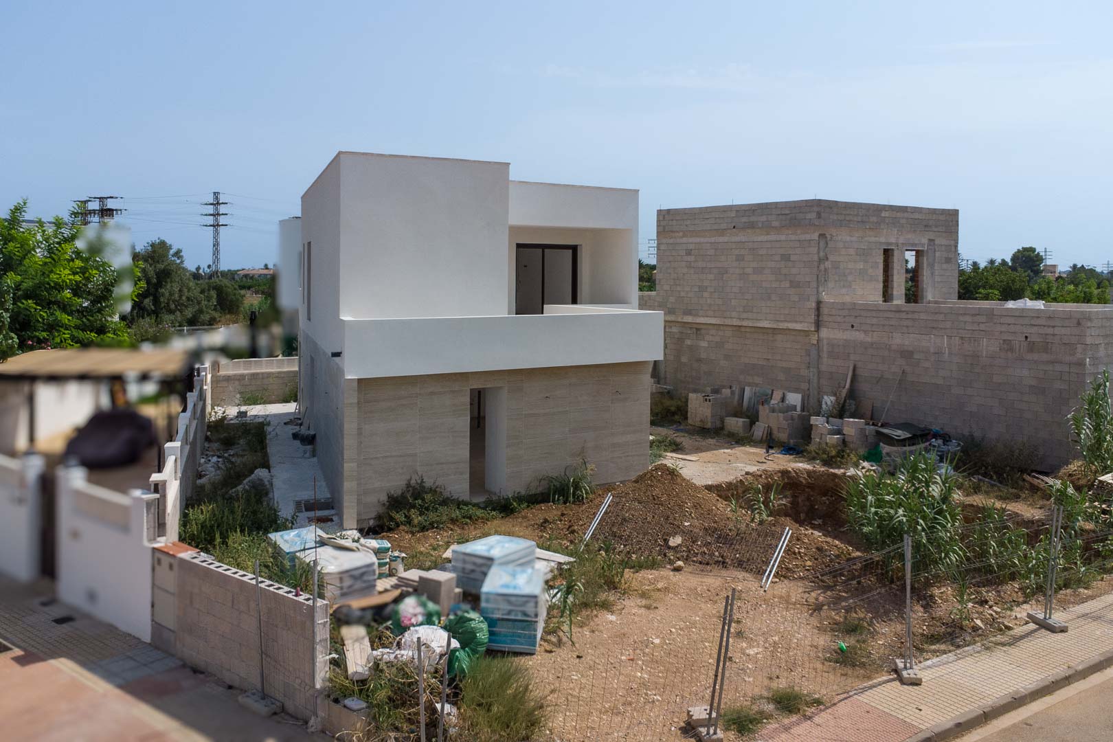 Vue extérieure de la villa en construction avec façade en pierre au rez-de-chaussée et étage blanc. Le terrain montre l'emplacement de la future piscine.
