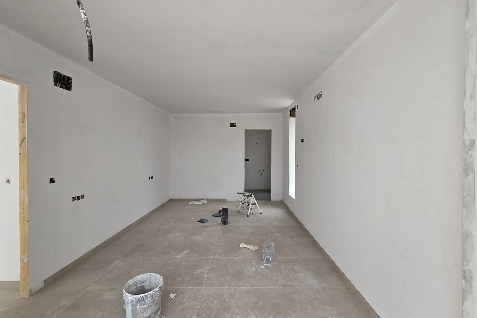 Vue intérieure en phase de finition avec un sol en grès cérame grand format et des murs blancs. Les pré-installations électriques et les accès aux pièces attenantes sont visibles.