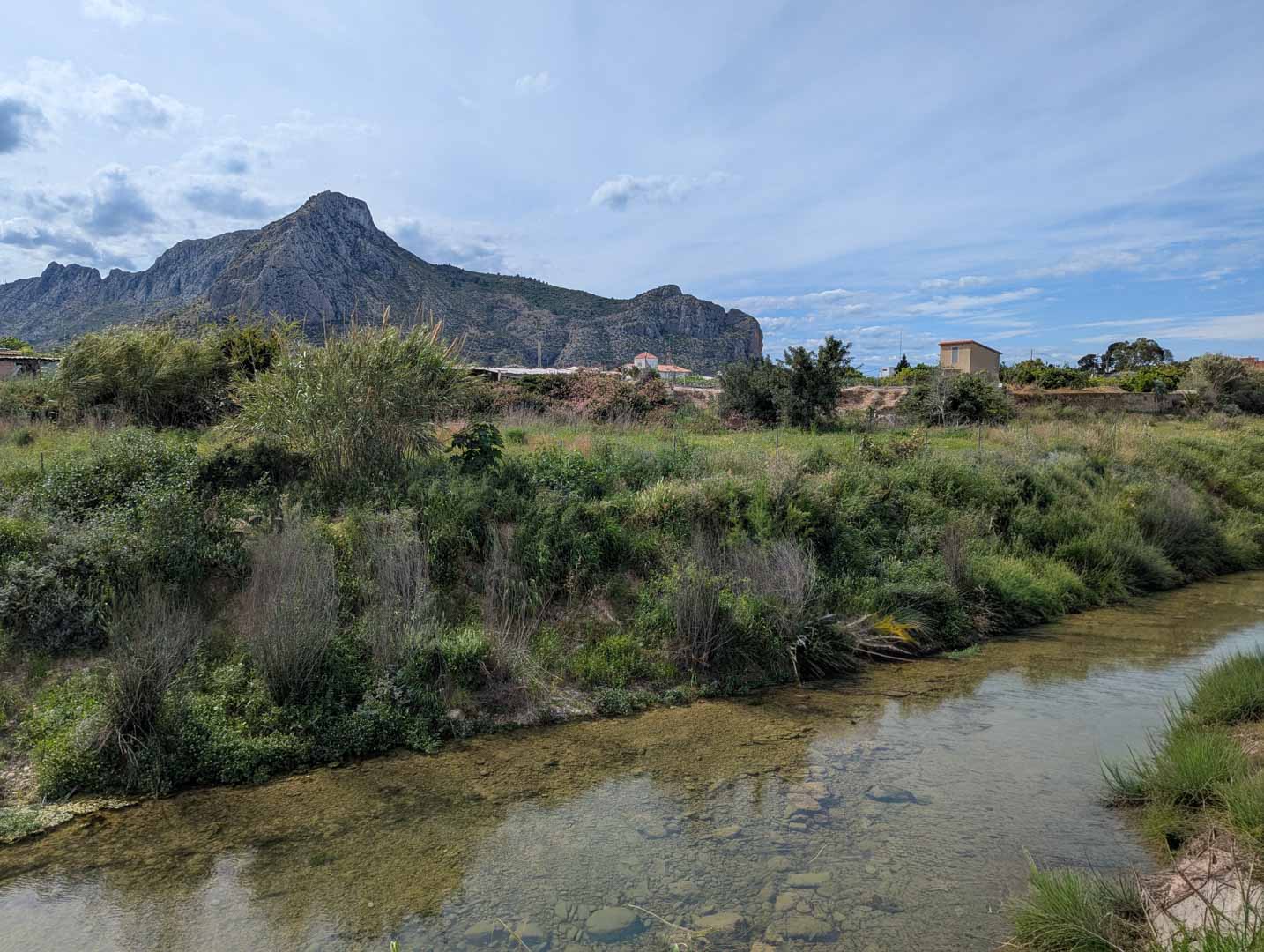 Vue sur l'environnement naturel avec un ruisseau aux eaux claires et une végétation sauvage, surplombé par les montagnes environnantes.